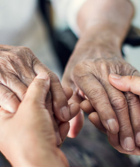 elderly woman and her caregiver holding hands