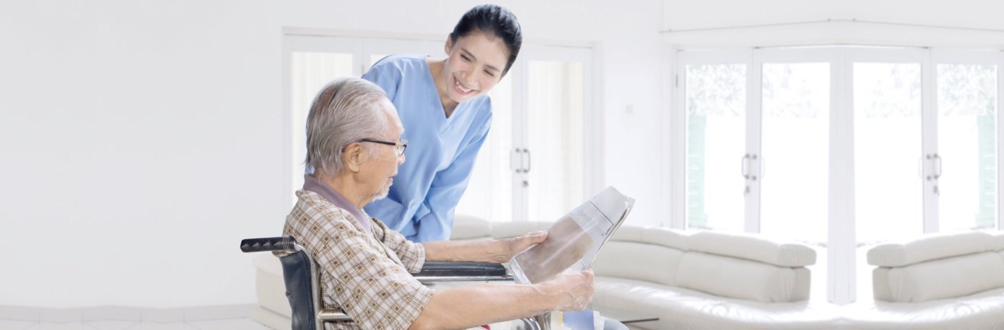 caregiver looking at the old man reading newspaper while smiling