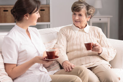 Friendly caregiver and smiling elderly woman drinking tea during meeting