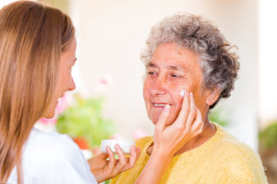 Caregiver rubs the face cream on the elderly womans face